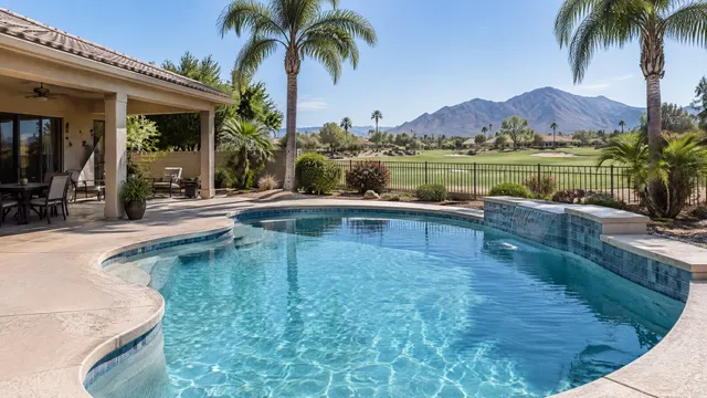 Backyard pool at a 1990s single-story home in east Mesa, Arizona: updated tile and coping, a covered patio, palm trees and a low wrought iron view fence looking toward a golf course, mountains on the horizon